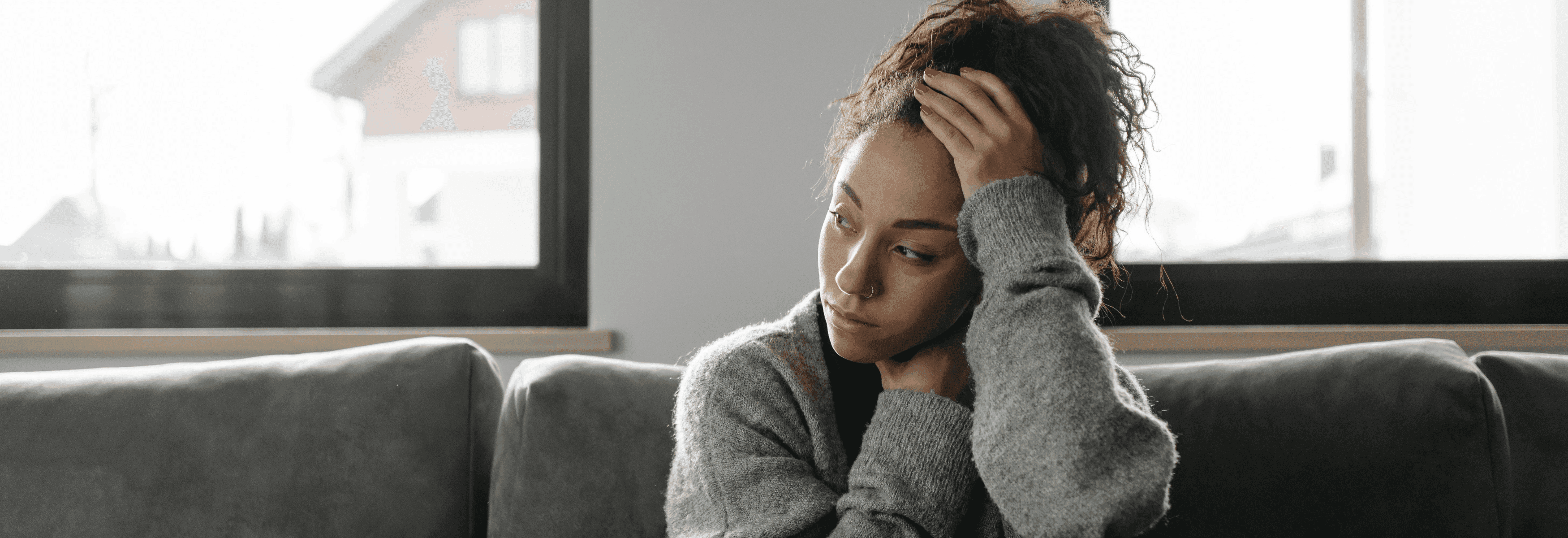 Nachdenkliche Frau sitzt auf einem Sofa und schaut aus dem Fenster